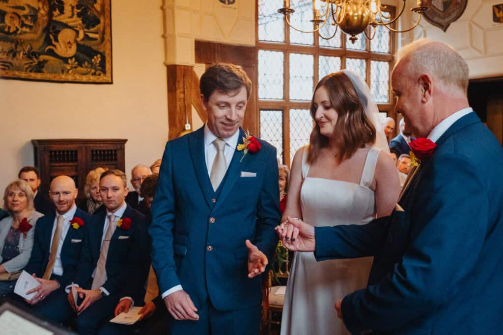 Emotional moment at Birtsmorton Court as the bride’s father hands over her hand to the groom during their intimate winter wedding ceremony. The stunning Cotswolds venue provides a romantic backdrop with its historic charm, warm candlelit ambiance, and heartfelt vows. A perfect capture of love, tradition, and family on their special day.