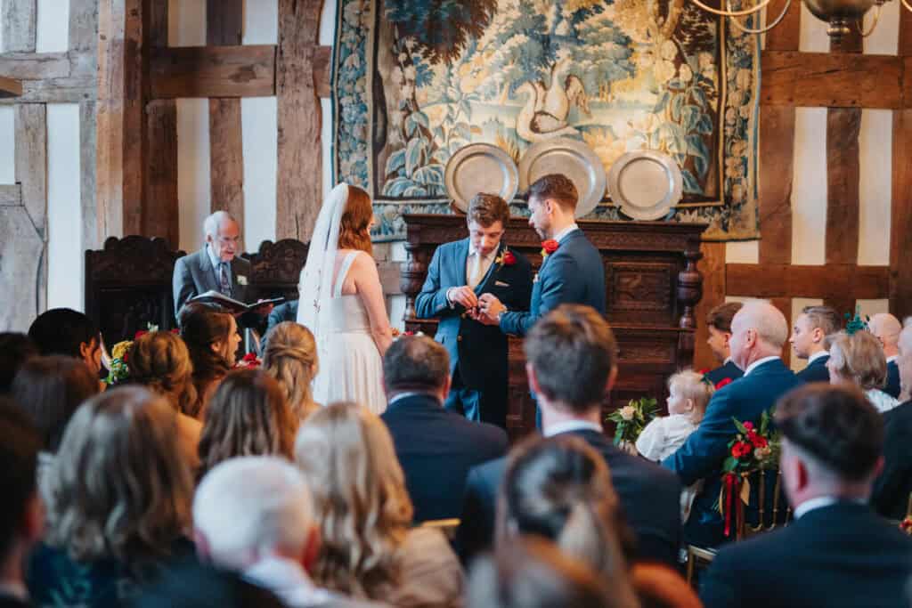 Emotional wedding ceremony at Birtsmorton Court as the groom places the wedding ring on his bride’s finger. Surrounded by family and friends in a stunning historic Cotswolds venue, the couple exchange vows in a warm, candlelit setting. The intimate moment is beautifully framed by the venue’s timber beams and intricate tapestries, capturing the essence of a romantic winter wedding. Expertly documented by a Buckinghamshire wedding photographer, specialising in natural and timeless wedding photography.