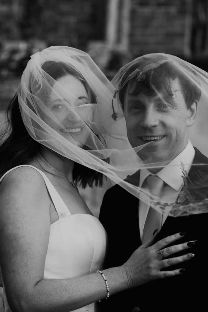 Romantic newlywed moment at Birtsmorton Court – the bride and groom share a joyful embrace under the bride’s delicate veil, their smiles radiating love and happiness. A timeless black and white wedding portrait capturing the essence of a winter wedding in the Cotswolds. Perfect for couples looking for elegant and emotive wedding photography inspiration.