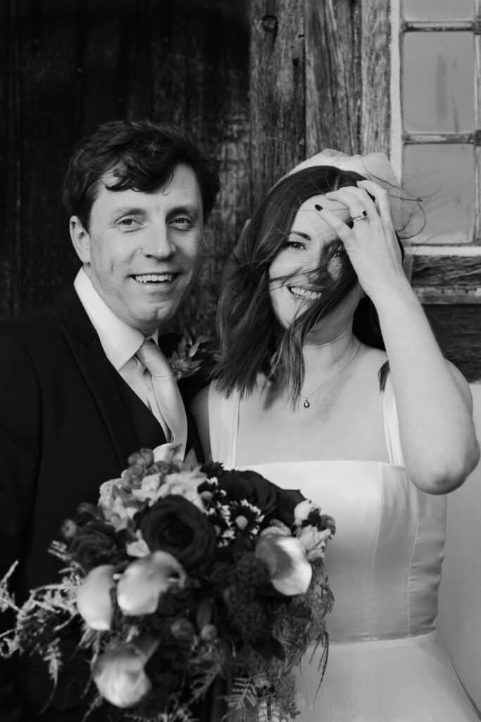 Candid black and white wedding portrait at Birtsmorton Court – the bride and groom share a joyful moment as the wind plays with her hair, capturing the beauty of love and laughter. A timeless and emotive image from a winter wedding in the Cotswolds, perfect for couples seeking natural and storytelling wedding photography.