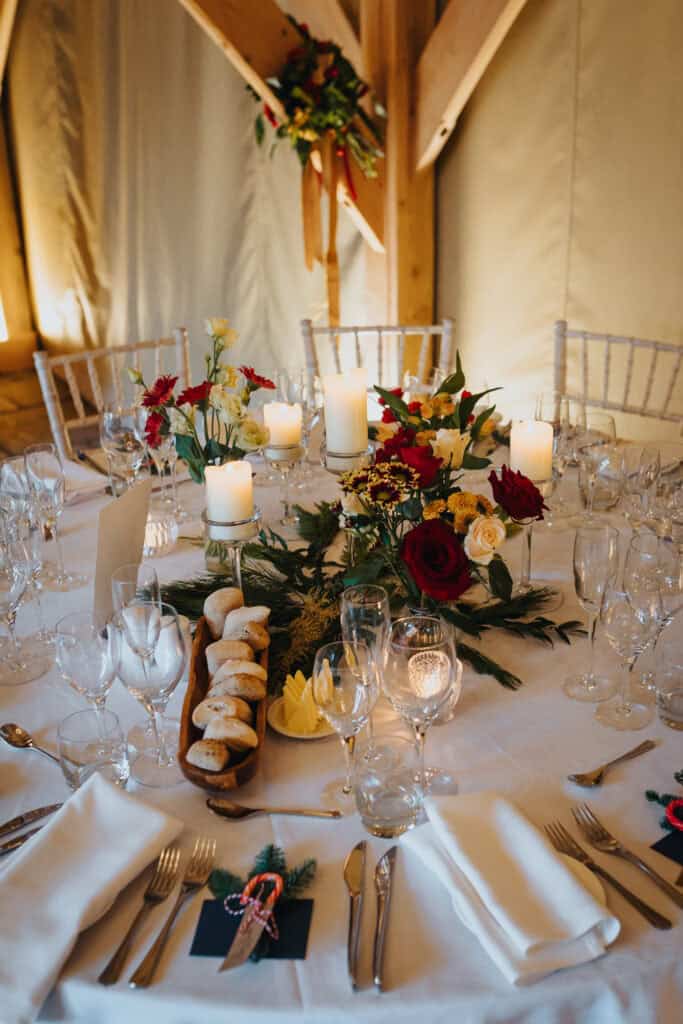 Stunning winter wedding table decor at Birtsmorton Court – a beautifully styled reception setup featuring elegant candlelit centrepieces, festive red and gold floral arrangements, and rustic touches. The perfect inspiration for couples planning a cosy yet sophisticated Cotswolds wedding celebration.