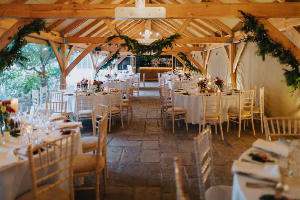 Elegant winter wedding reception at Birtsmorton Court – a beautifully decorated barn venue featuring candlelit tables, festive floral arrangements, and rustic charm. The warm wooden beams adorned with greenery create a magical setting for a cosy Cotswolds wedding celebration.