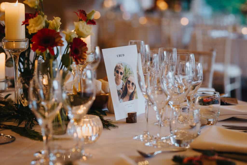 Elegant winter wedding table setting at Birtsmorton Court – candlelit ambiance, personalised travel-themed table names, and beautifully arranged floral centrepieces with deep red and ivory tones. A perfect blend of romance and sophistication for a cosy Cotswolds wedding reception.