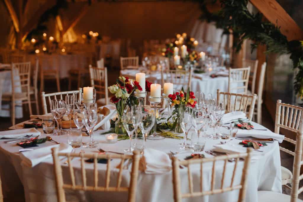 Romantic winter wedding reception at Birtsmorton Court – candlelit tables adorned with elegant floral arrangements in deep red and ivory hues. A warm and intimate setting for a magical Cotswolds wedding, capturing the essence of timeless elegance and festive charm.
