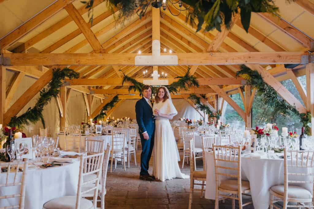 Newlyweds at their romantic winter wedding reception at Birtsmorton Court. The beautifully decorated barn, adorned with festive greenery and candlelit tables, sets the perfect scene for an intimate Cotswolds wedding celebration. A dreamy setting for timeless wedding photography.