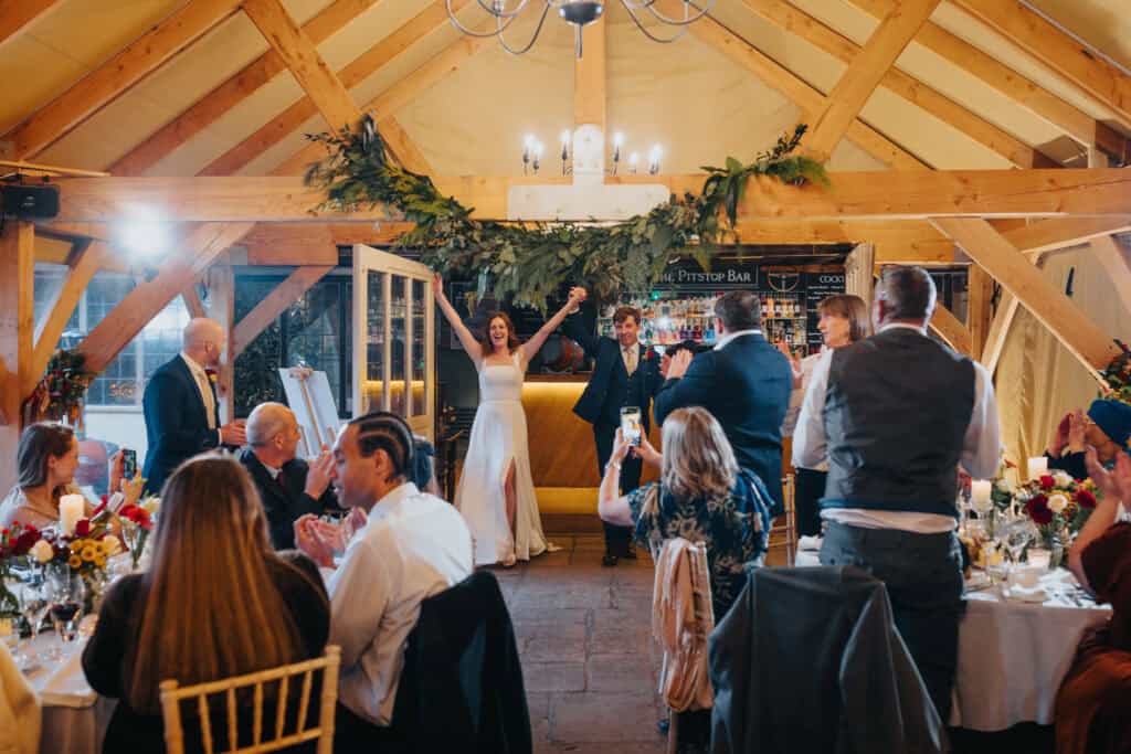 Newlyweds' grand entrance at Birtsmorton Court wedding reception – the bride and groom celebrate with joyous cheers from their guests in a beautifully decorated winter wedding venue. A magical Cotswolds celebration filled with love, laughter, and elegant rustic charm.