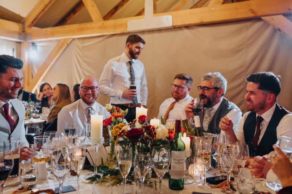 Lively wedding reception at Birtsmorton Court – a candid moment of laughter and camaraderie among guests during a winter wedding celebration. The warm glow of candlelight, elegant floral centrepieces, and a joyful atmosphere make this a perfect inspiration for couples planning a relaxed and fun-filled wedding in the Cotswolds.