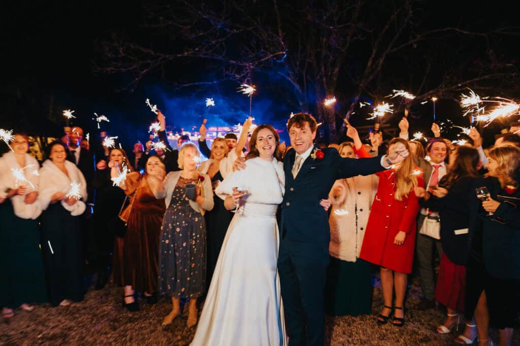 Festive sparkler send-off at Birtsmorton Court – the bride and groom celebrate their magical winter wedding surrounded by loved ones under the night sky. A stunning and joyful moment filled with warm lights and happy faces, creating unforgettable wedding photography in the Cotswolds.