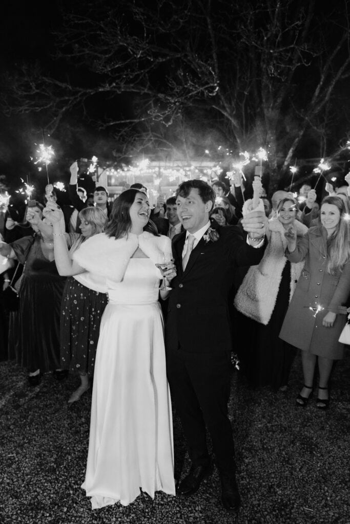 Elegant black and white sparkler exit at Birtsmorton Court – the bride and groom share a joyful moment surrounded by loved ones in a magical winter wedding celebration. A timeless and romantic wedding photography capture, perfect for couples looking for classic and emotive wedding inspiration.