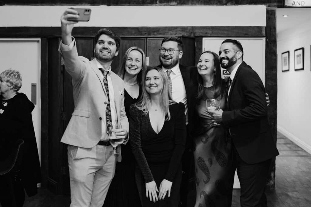 Candid wedding guest selfie at Birtsmorton Court – a joyful group of friends captures a fun moment during a winter wedding celebration. A stylish black and white wedding photography shot showcasing the excitement and togetherness of the evening reception.