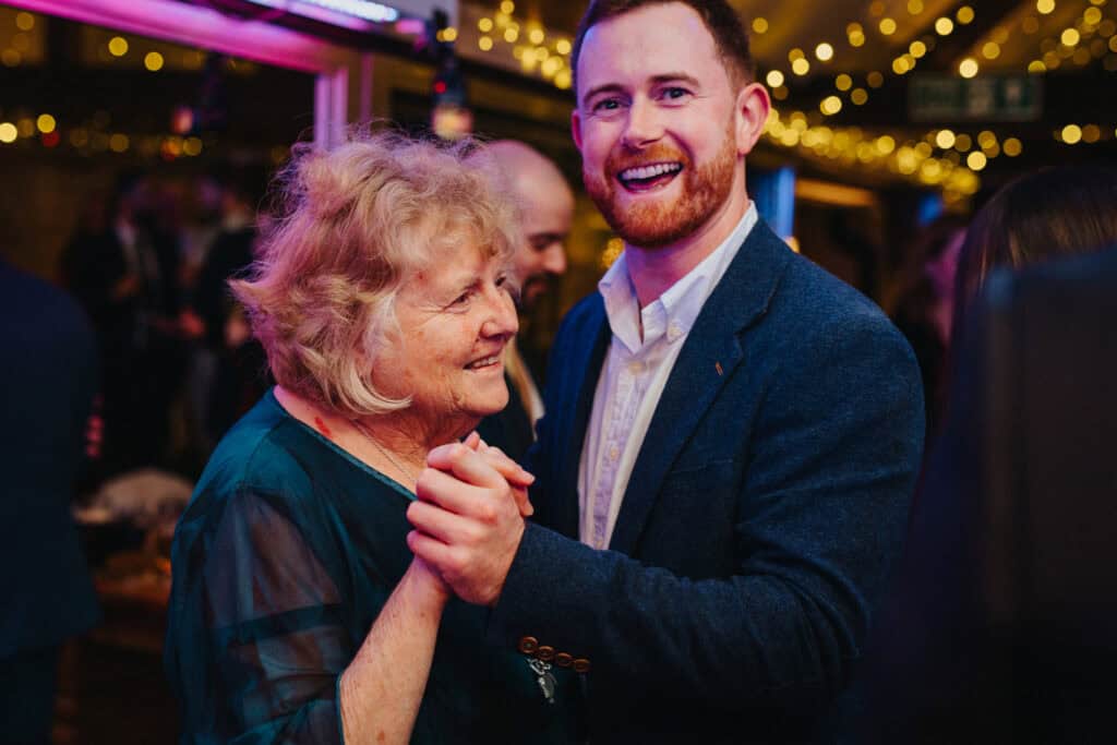 Heartwarming moment on the dance floor at Birtsmorton Court – a joyful wedding guest shares a dance with a loved one during the evening celebrations. Twinkling fairy lights and a warm atmosphere set the scene for a magical winter wedding party in the Cotswolds.