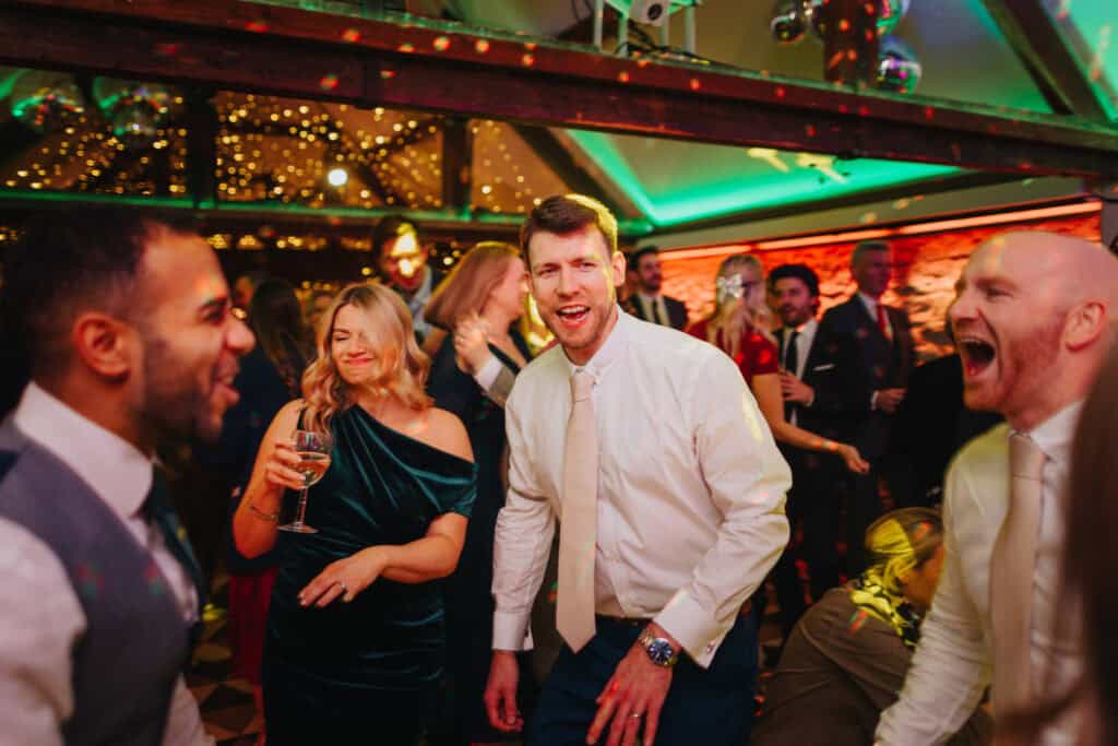 Lively evening party at a winter wedding at Birtsmorton Court. Guests celebrating on the dance floor with music, laughter, and festive lighting, capturing the joy of a Cotswolds wedding reception.