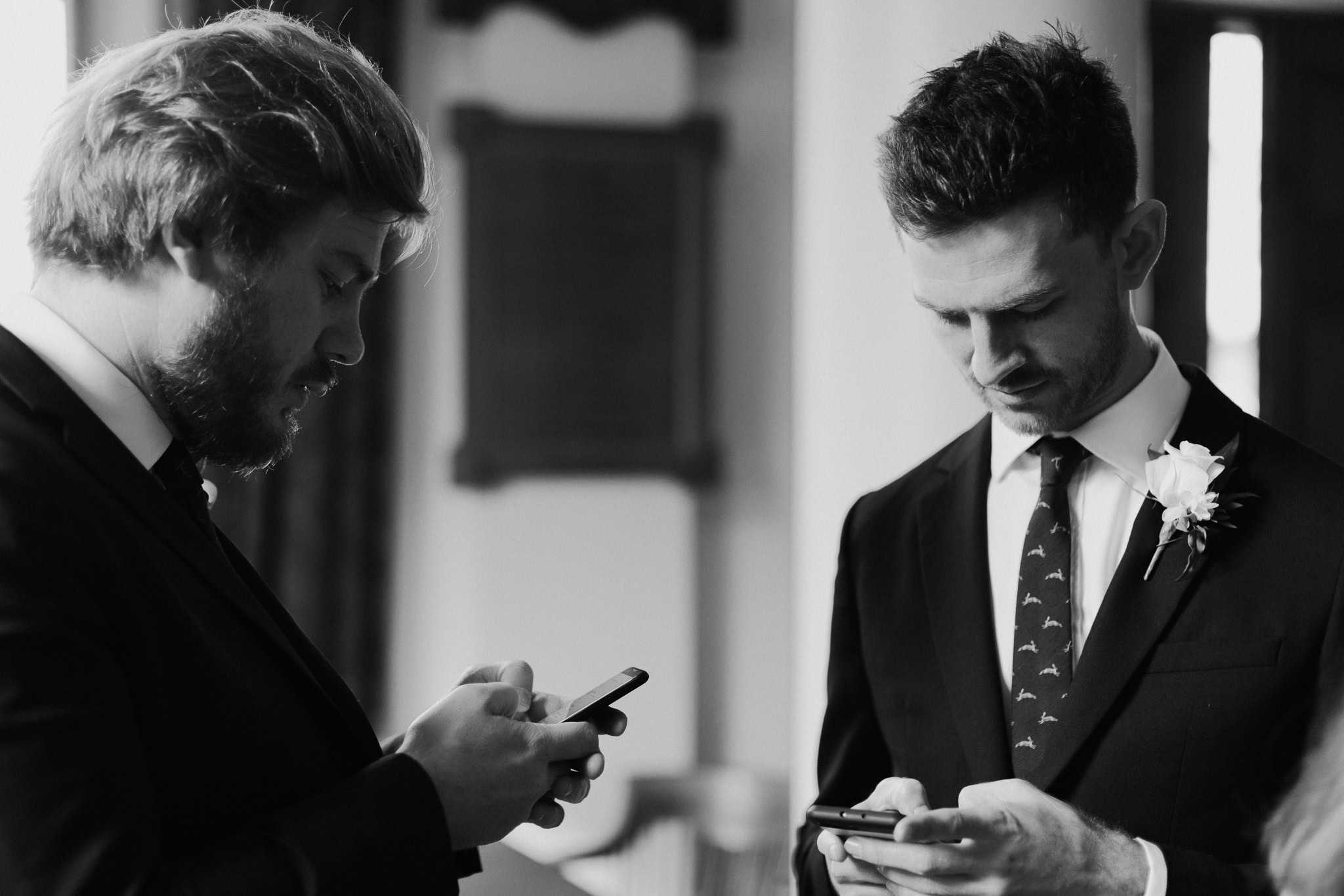 Black and white candid shot of groom and best man checking their phones before the wedding ceremony at Woodstock Town Hall. A relaxed and modern wedding moment captured beautifully.