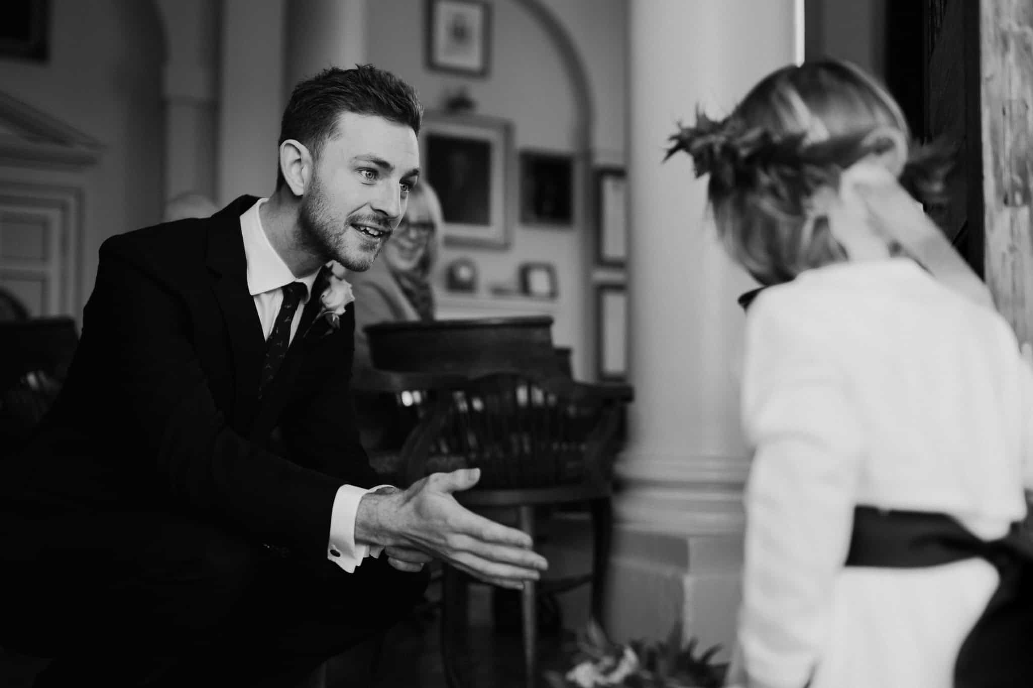 Black and white candid photo of the groom warmly greeting the flower girl before the ceremony at Woodstock Town Hall. A touching and joyful wedding moment captured beautifully.