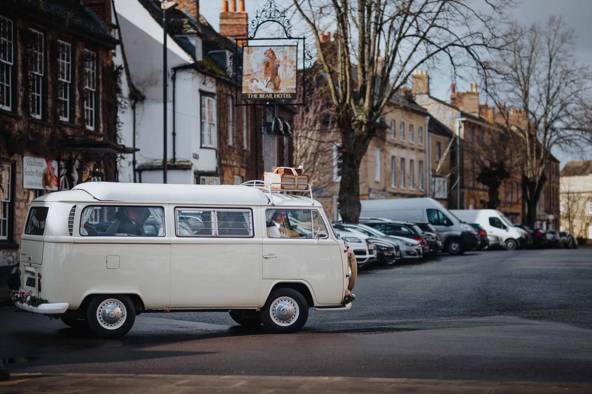 A beautifully decorated vintage VW camper van arrives at The Bear Hotel, Woodstock, for a wedding reception. A stylish and timeless wedding transport choice captured in a charming Cotswolds setting.