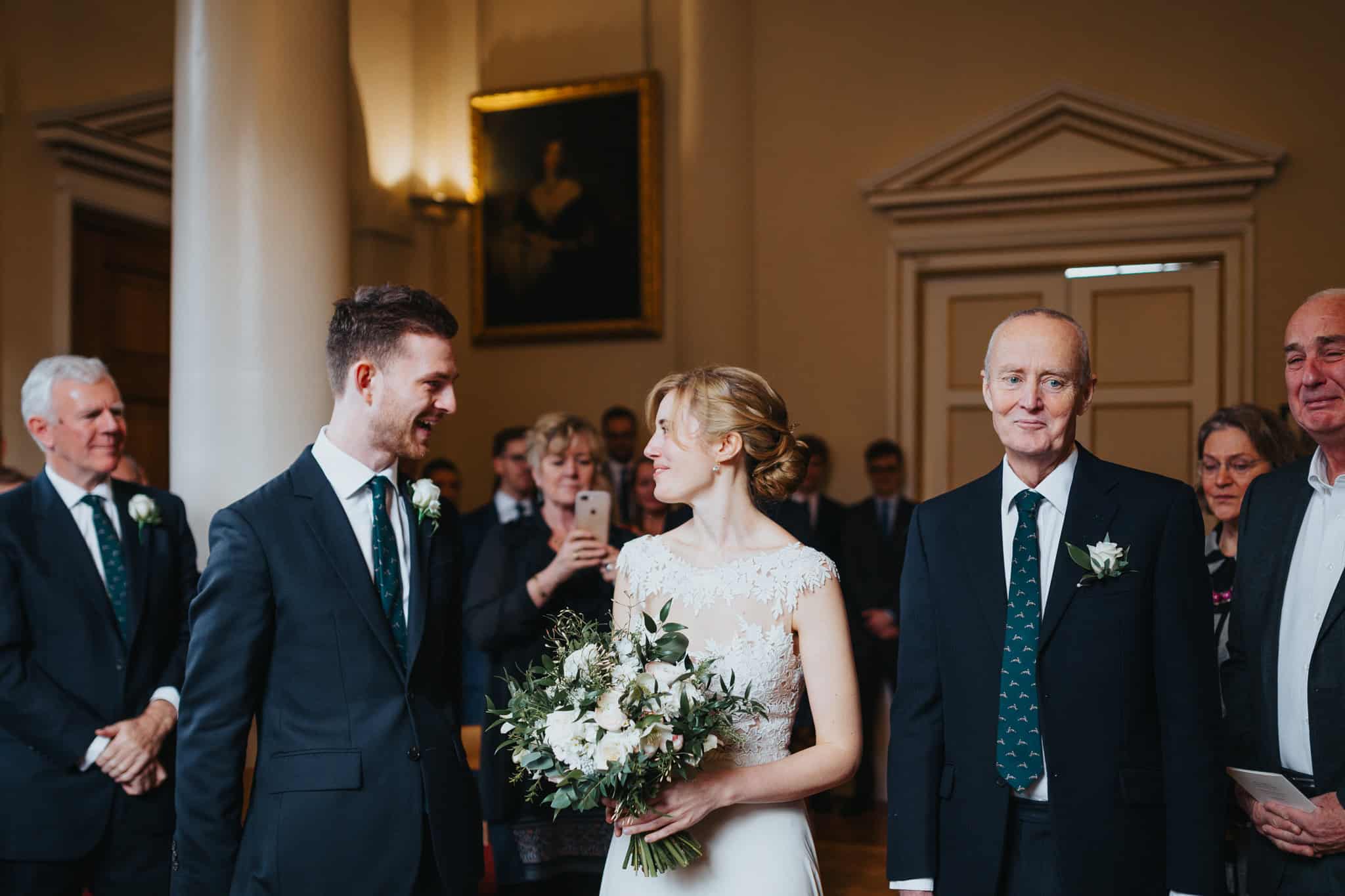 A joyful moment as the bride walks down the aisle at Woodstock Town Hall, meeting the groom with a smile. A heartwarming wedding ceremony scene filled with love and emotion.