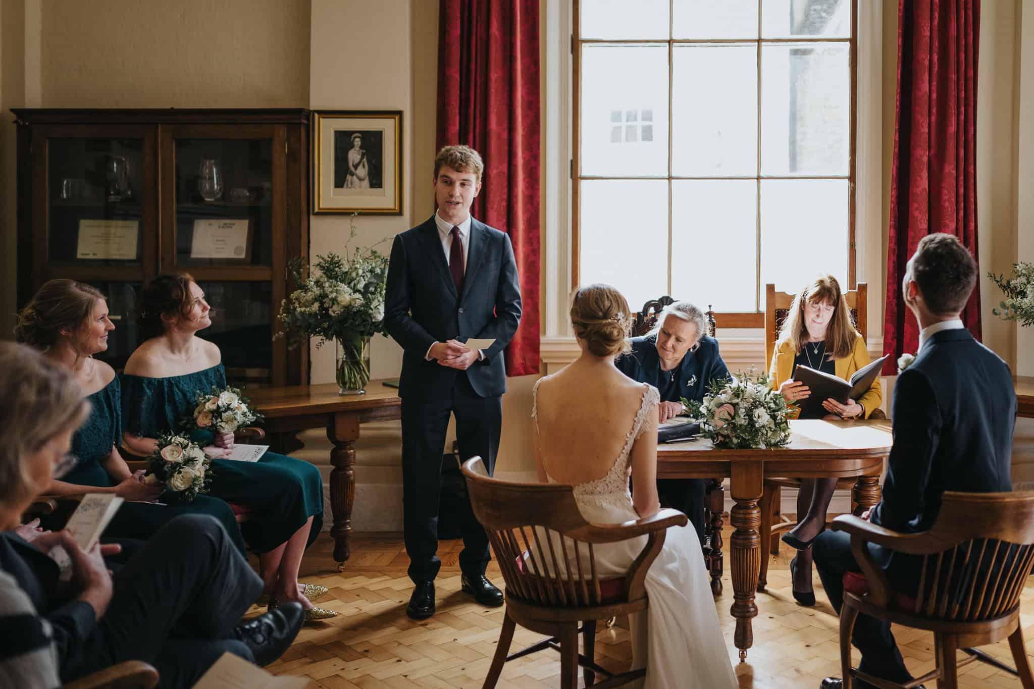 A heartfelt wedding ceremony at Woodstock Town Hall, with the bride and groom seated as a guest delivers a speech. A beautifully captured candid moment filled with love and emotion.