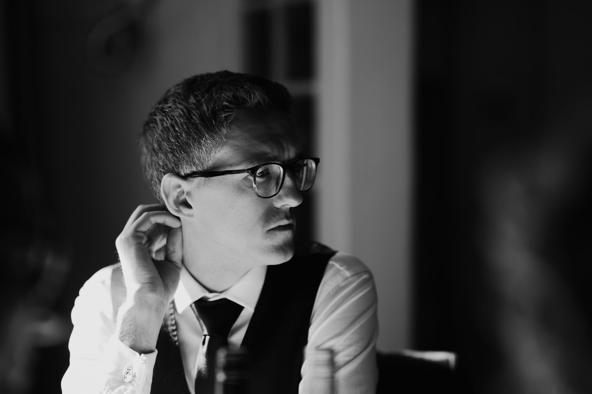 A candid black and white portrait of a wedding guest in glasses, deep in thought at Alice and Kit’s wedding reception at Macdonald Bear Hotel, Woodstock. Capturing real moments in wedding photography.