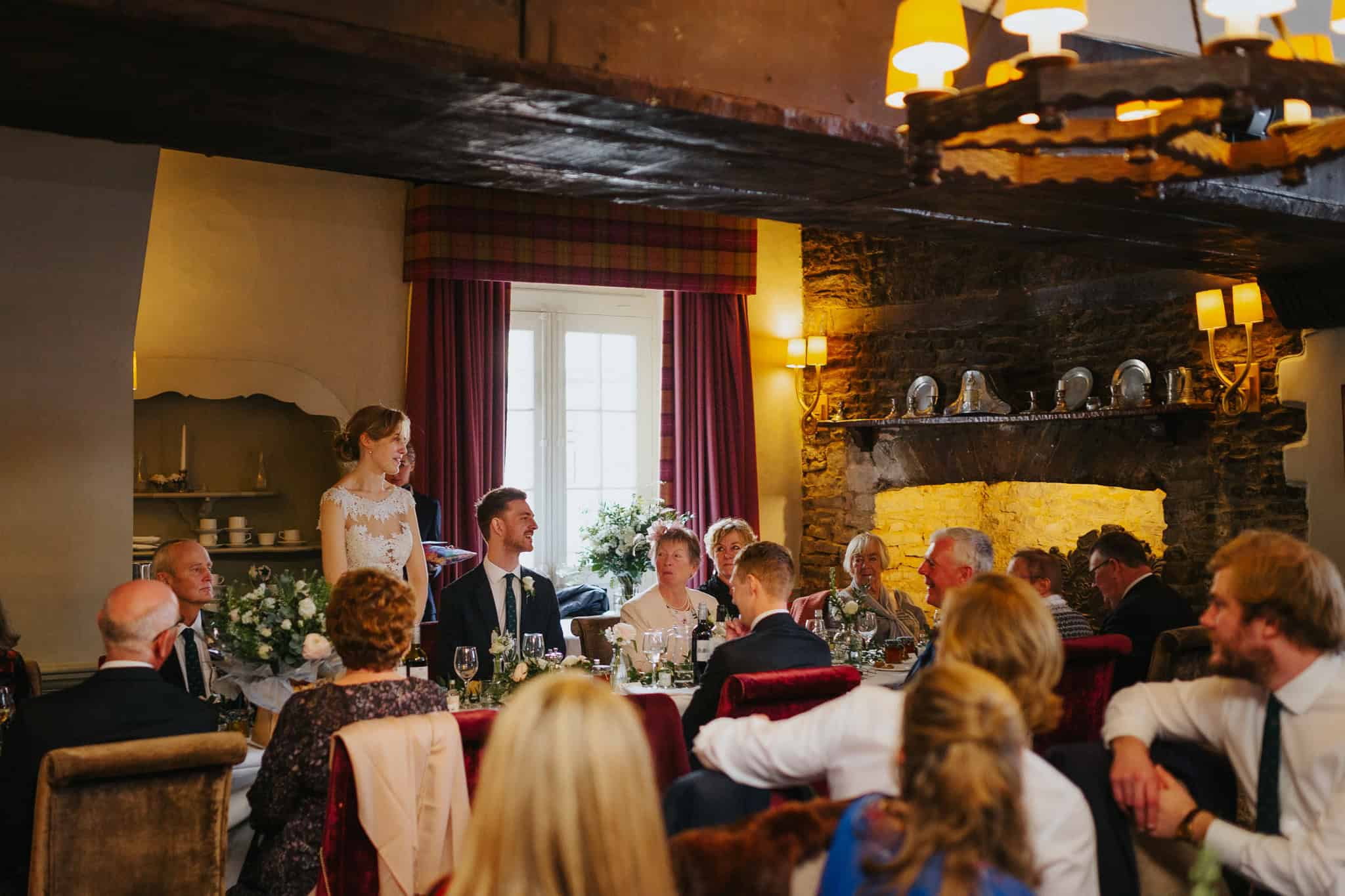 The bride delivers an emotional wedding speech at Macdonald Bear Hotel, Woodstock, with guests warmly listening. A beautifully intimate moment during the reception in a rustic, candlelit setting.