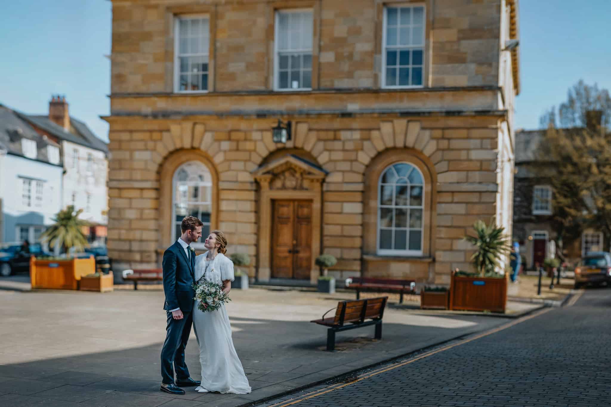 Newlyweds share a tender moment outside Woodstock Town Hall, Oxfordshire, after their ceremony. A beautifully captured wedding portrait with historic architecture in the background.