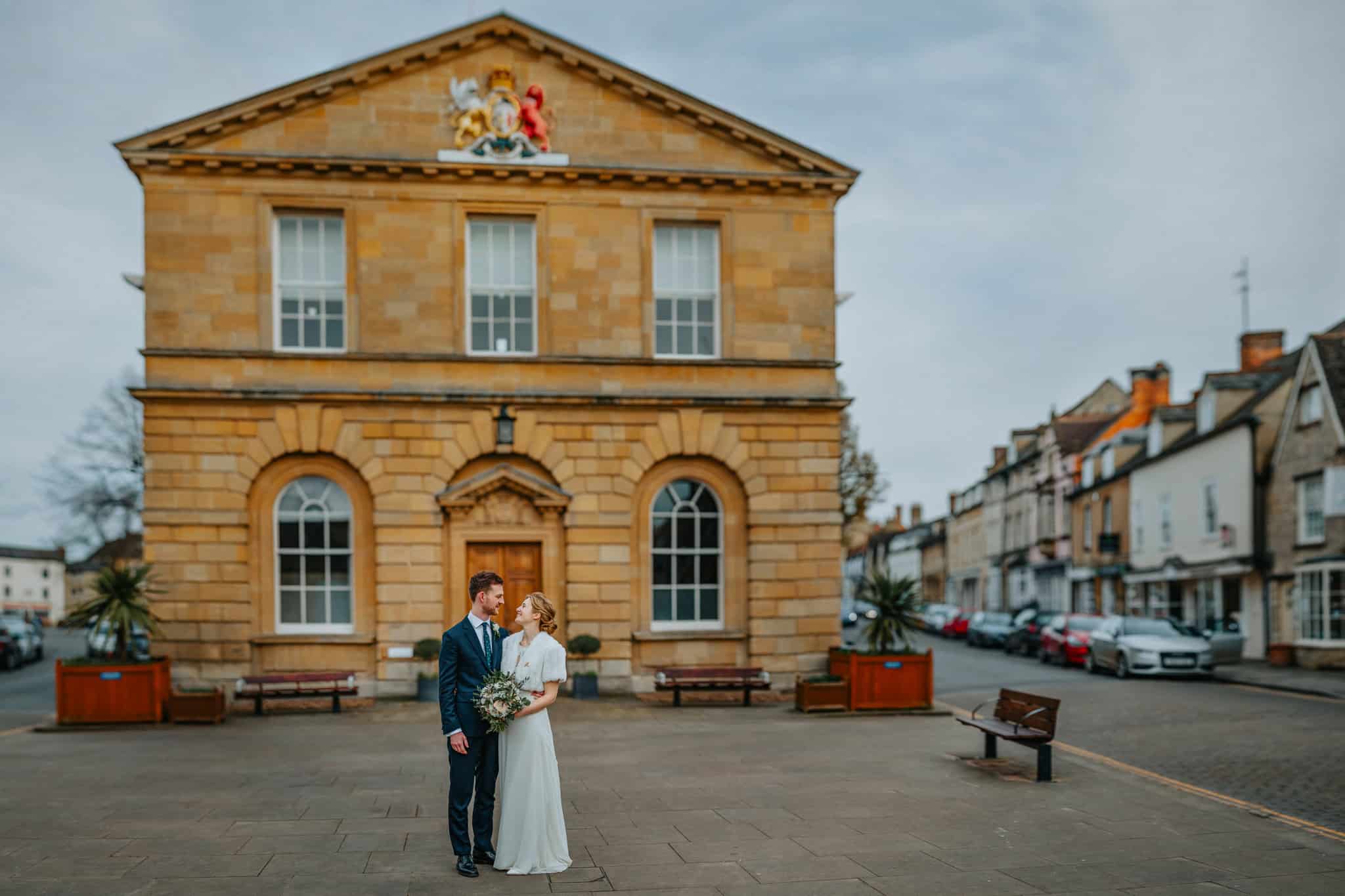 Bride and groom share a romantic moment in front of the historic Woodstock Town Hall in Oxfordshire, beautifully capturing their wedding day in a timeless and elegant setting.