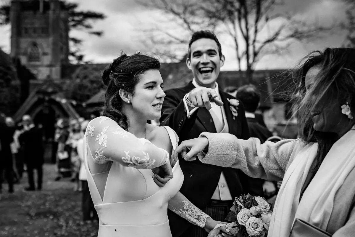 The bride pulls confetti from her bra, just as the groom spots the photographer capturing the moment – and points with a knowing smile. A perfectly timed, cheeky scene that says it all about fun, relaxed weddings.