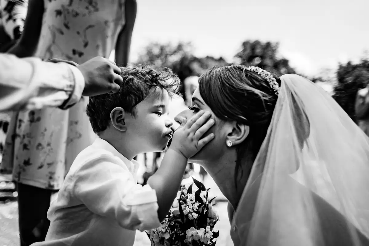 A heartwarming scene as a young boy gently holds the bride’s face for a kiss. Captured in a quiet, candid moment full of emotion and connection.