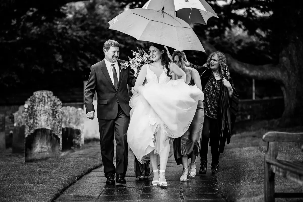 A beautiful documentary moment as the bride walks to the church under umbrellas, supported by family and friends. A perfect example of grace, laughter and togetherness in unexpected weather.