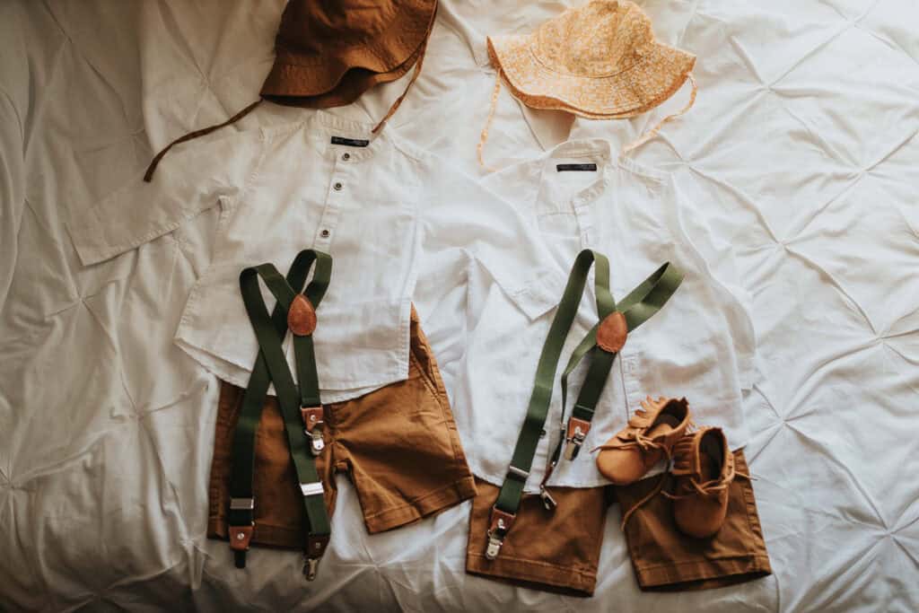Adorable summer wedding attire for children, featuring earthy tones and rustic charm. The outfit includes light cotton white shirts, mustard-brown shorts, green suspenders, stylish sun hats, and matching moccasin shoes – perfect for a farm marquee wedding!