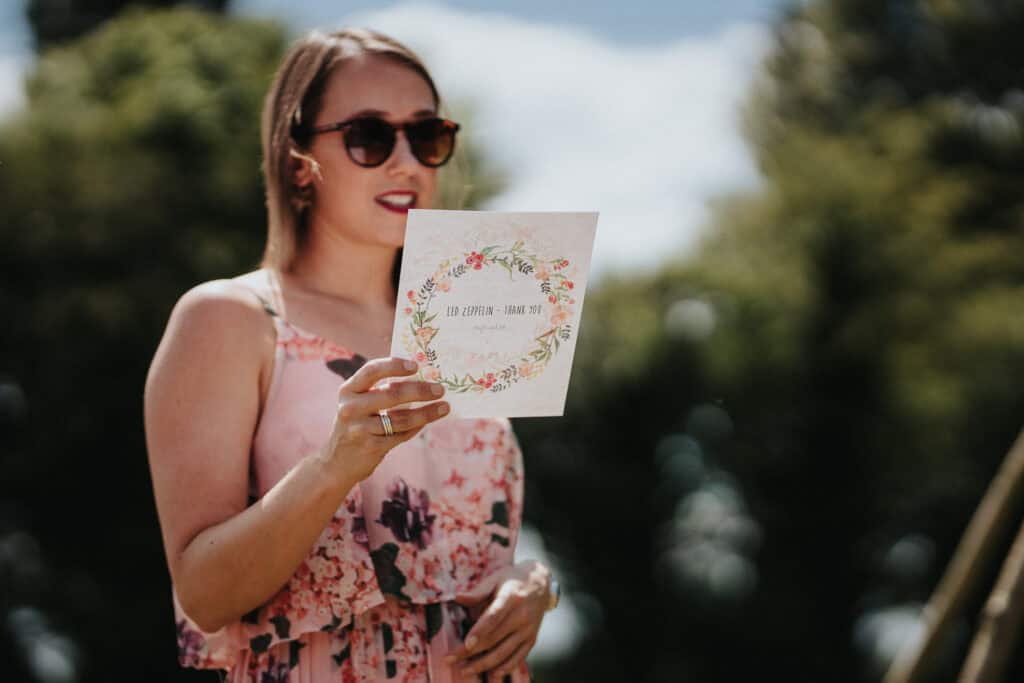 Wedding guest delivering a heartfelt speech under sunny skies, holding a floral-themed card during an outdoor celebration.