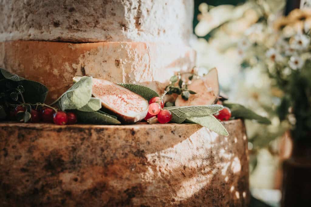 Close-up of a rustic cheese wheel display decorated with fresh figs, red berries, and green foliage, creating a natural and elegant setting in soft, ambient lighting.