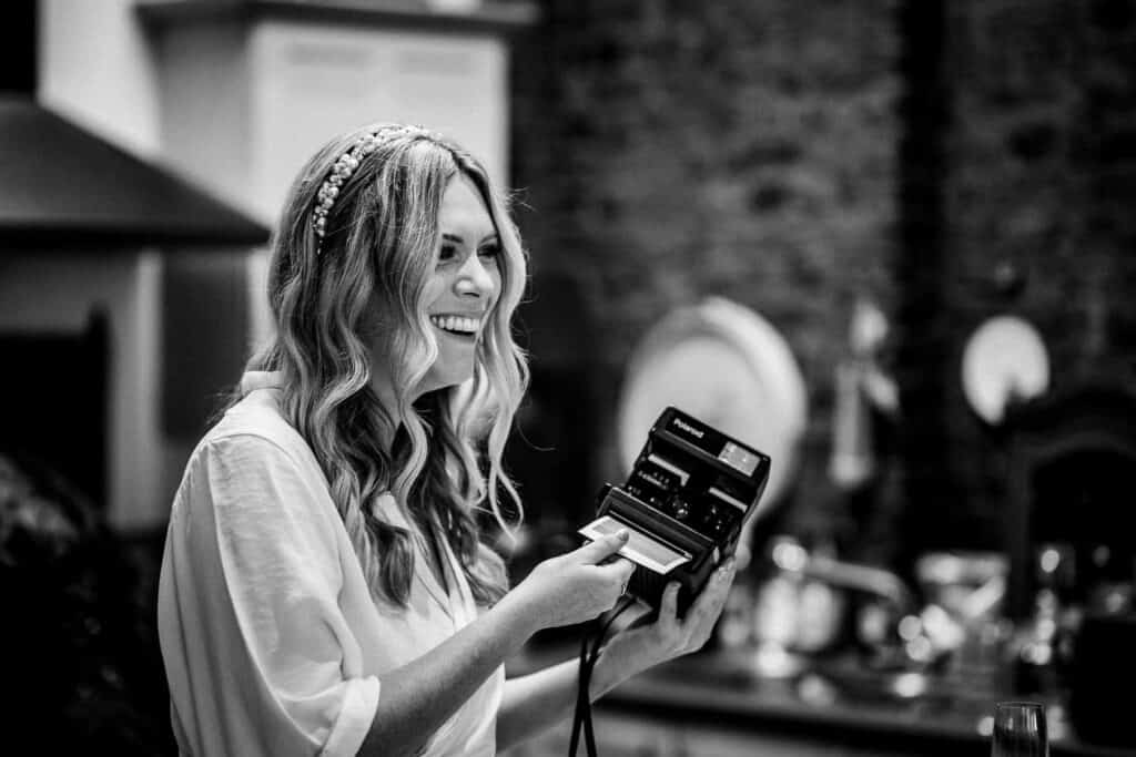 panna młoda podczas przygotowań ślubnych trzyma aparat Polaroid i uśmiecha się przed ceremonią