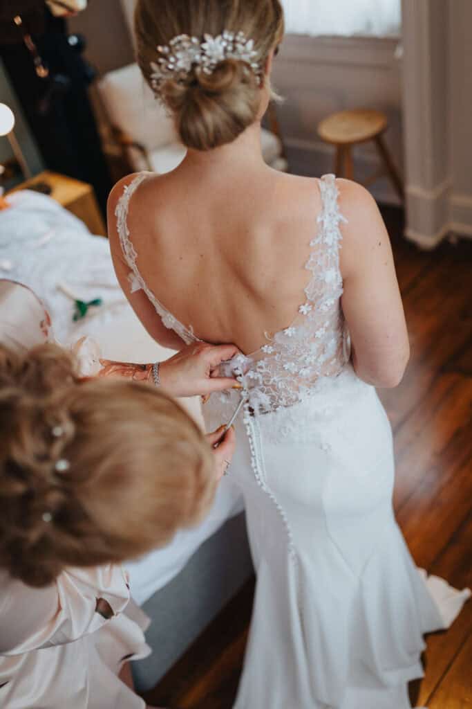 Close-up of bride’s lace wedding dress being buttoned during morning preparations at Thorpe Garden winter wedding, with a delicate hairpiece and soft bridal hairstyle.
