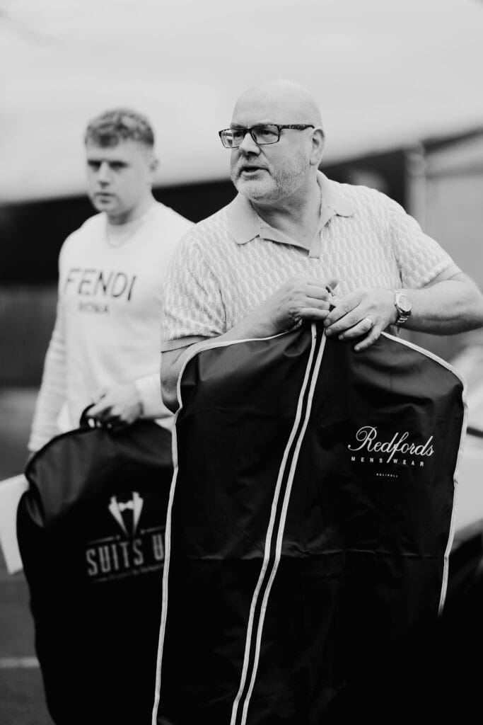 Father of the bride and groomsman carrying suit bags during wedding morning preparations at Thorpe Garden, getting ready for the winter ceremony.