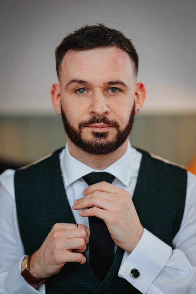 Close-up of the groom adjusting his black tie while getting ready for a winter wedding at Thorpe Garden, Staffordshire.