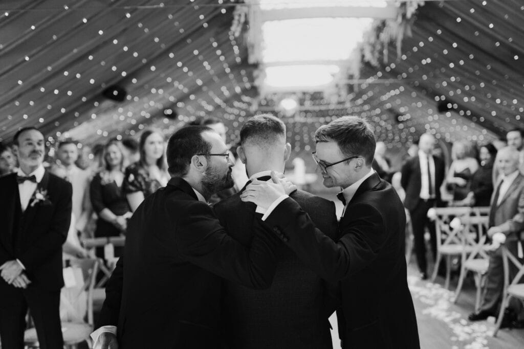Groom receiving final words and support from his brother and best man before the wedding ceremony at Thorpe Garden, Staffordshire, surrounded by guests and fairy lights.