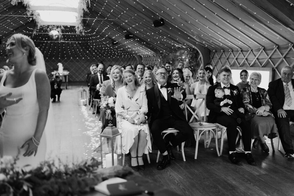 Family and guests laughing and enjoying a candid moment during the wedding ceremony at Thorpe Garden in Staffordshire.