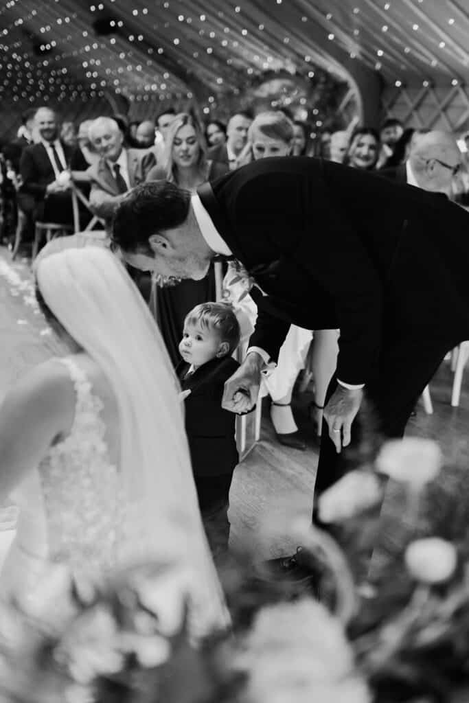 The bride's young son as the ring bearer holding hands with a guest during the wedding ceremony at Thorpe Garden, Staffordshire.