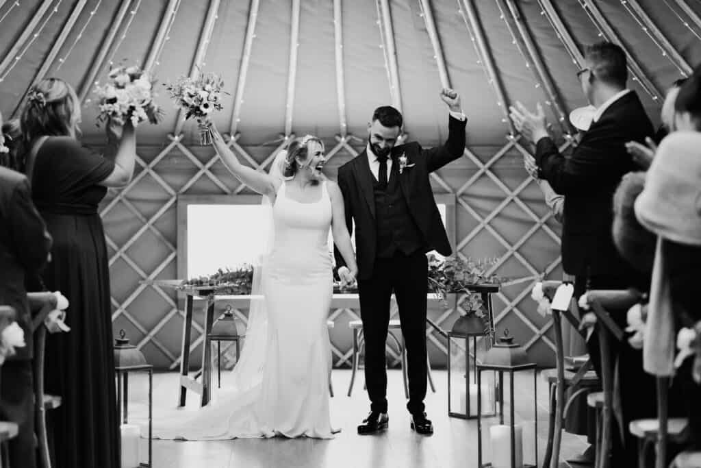 Bride and groom raise their arms in celebration after being announced as married during their winter wedding ceremony at Thorpe Garden, Staffordshire.