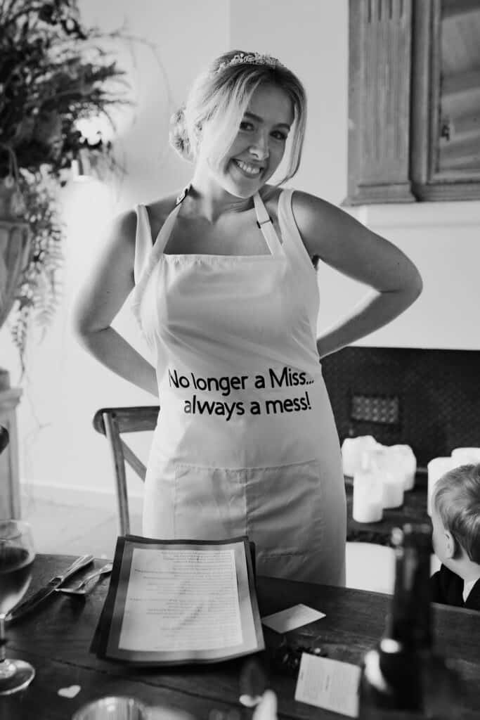 Bride at Thorpe Garden wedding wearing apron with “No longer a Miss… always a mess!” printed on it, smiling during the wedding breakfast.
