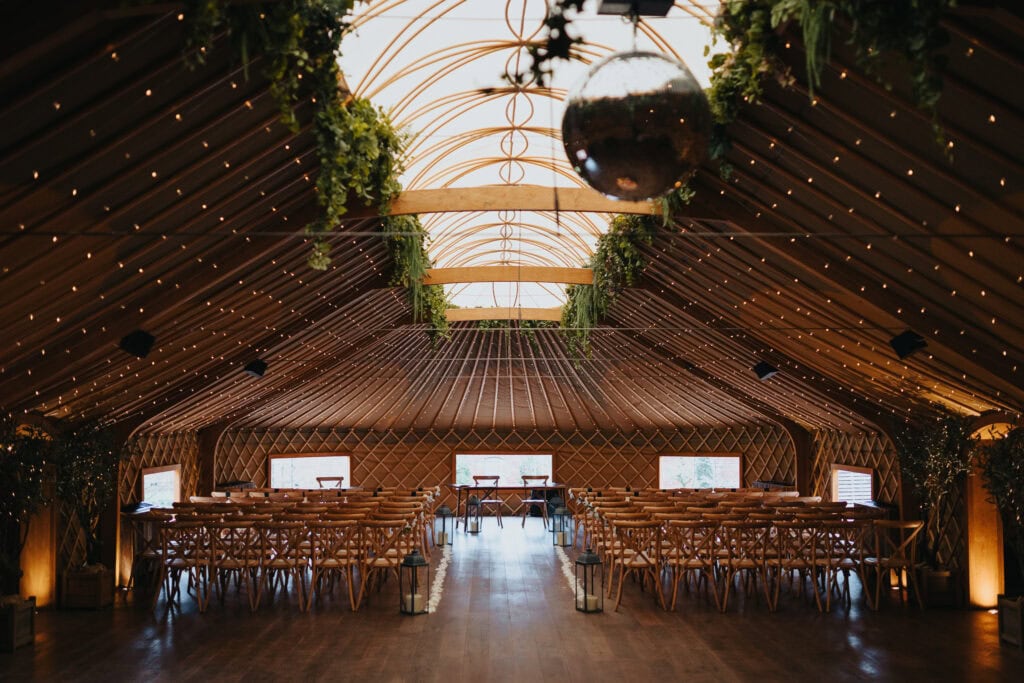 Wedding ceremony setup inside the Thorpe Garden yurt with wooden chairs, greenery, fairy lights, and a disco ball ready for a winter wedding.